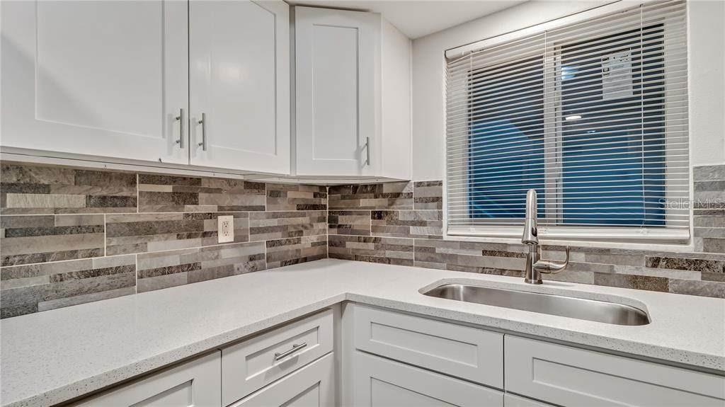 A kitchen features white cabinets, a light-colored quartz countertop, and a multi-toned stone tile backsplash — 5900 22ND AVENUE N UNIT 8, ST PETERSBURG, FL