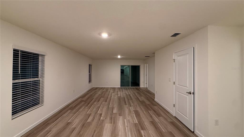 An empty room features light wood-look flooring, white walls, and a sliding glass door — 7749 SW 46TH COURT, OCALA, FL