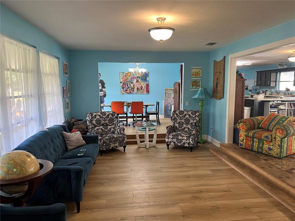 A living room with blue walls, wood-look flooring, and a raised dining area in the background — 25446 SW 5 AVENUE, NEWBERRY, FL