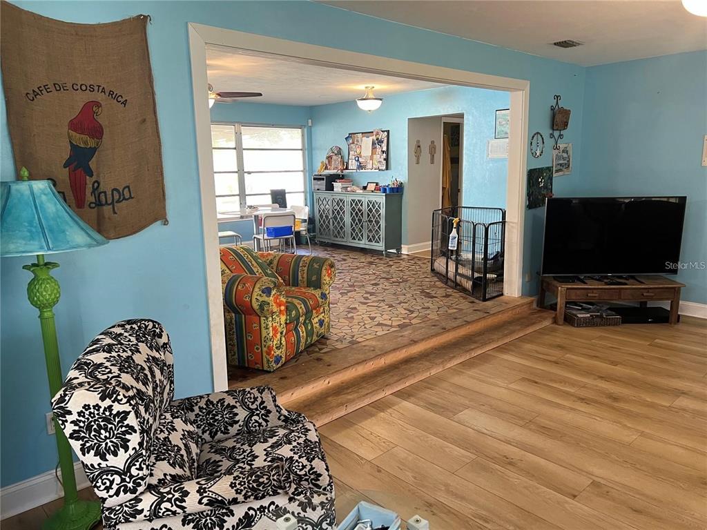 A living room with light blue walls, wood-look flooring, and a step up to a tiled area — 25446 SW 5 AVENUE, NEWBERRY, FL