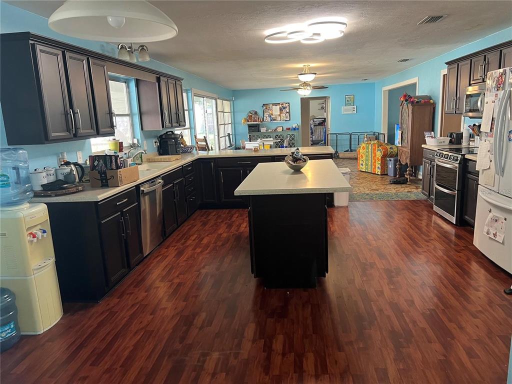 A kitchen features dark cabinetry, a central island, and wood-look flooring under light blue walls — 25446 SW 5 AVENUE, NEWBERRY, FL