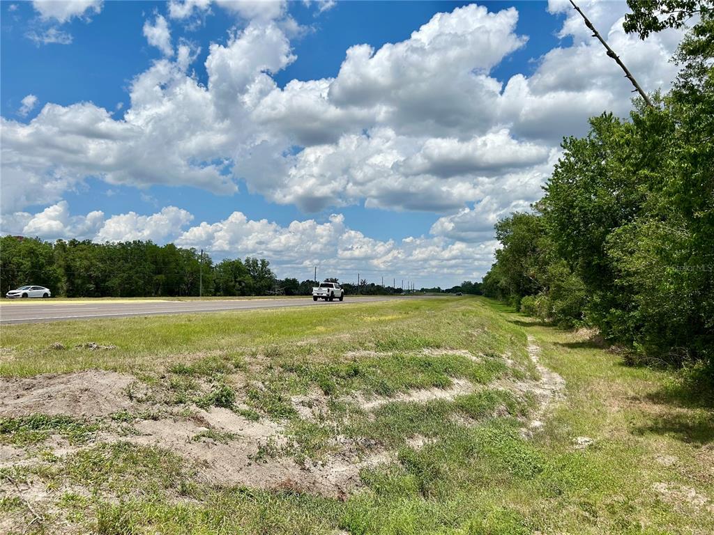 A grassy roadside lot with trees borders a paved highway under a cloudy blue sky — BRONCO DRIVE, ZOLFO SPRINGS, FL