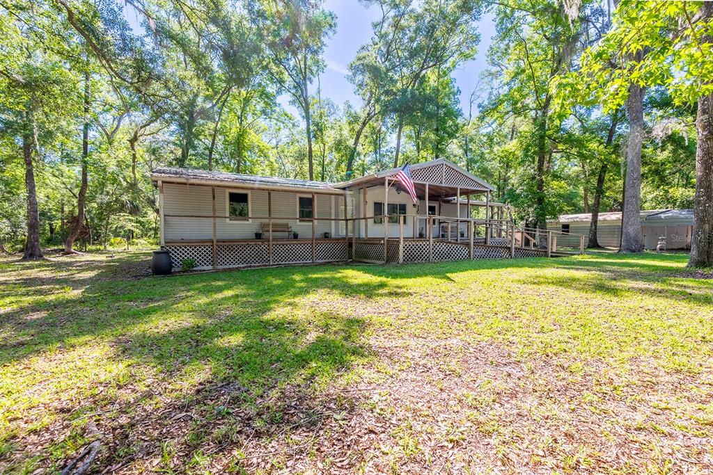 A single-story house with a large wooden deck and an American flag stands among trees — 343 NE 743RD STREET, OLD TOWN, FL