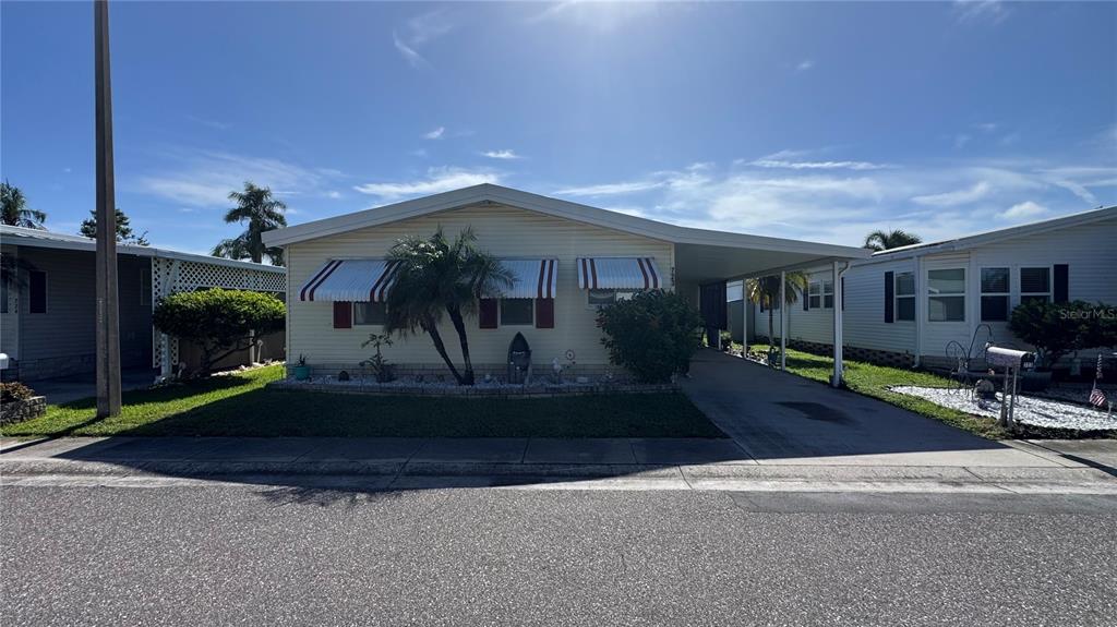 A single-story mobile home with a carport and red-and-white striped window awnings — 1001 STARKEY ROAD UNIT 723, LARGO, FL
