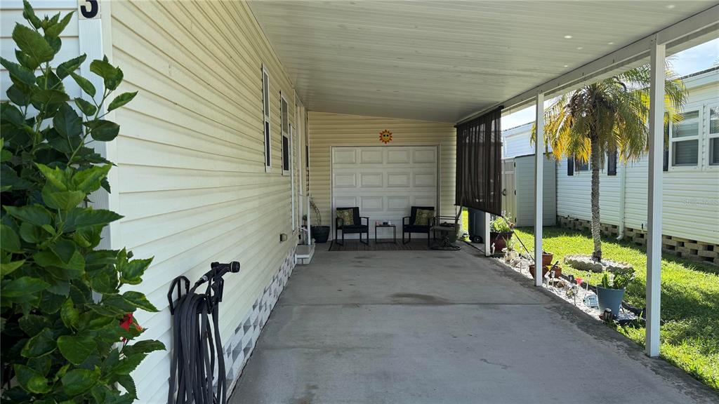 A covered concrete carport features a white garage door, two chairs, and a small table — 1001 STARKEY ROAD UNIT 723, LARGO, FL