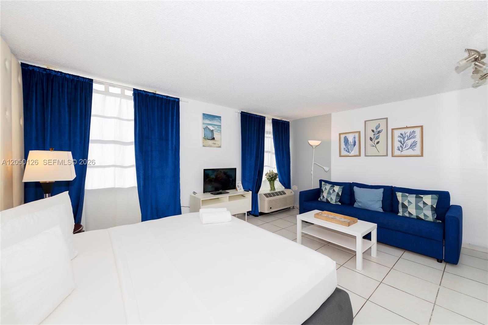 A bedroom with a bed, blue sofa, white tile floors, and blue curtains — 710 Washington Ave # 414, Miami Beach FL 33139, MIAMI BEACH, FL
