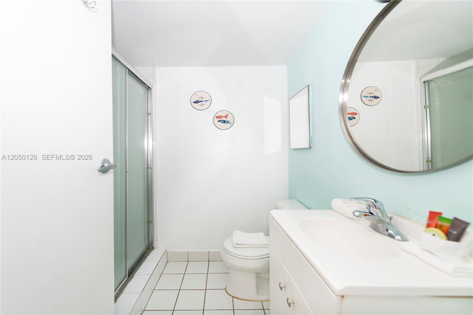 A bathroom features a white vanity, a toilet, a glass-enclosed shower, and light blue walls — 710 Washington Ave # 414, Miami Beach FL 33139, MIAMI BEACH, FL