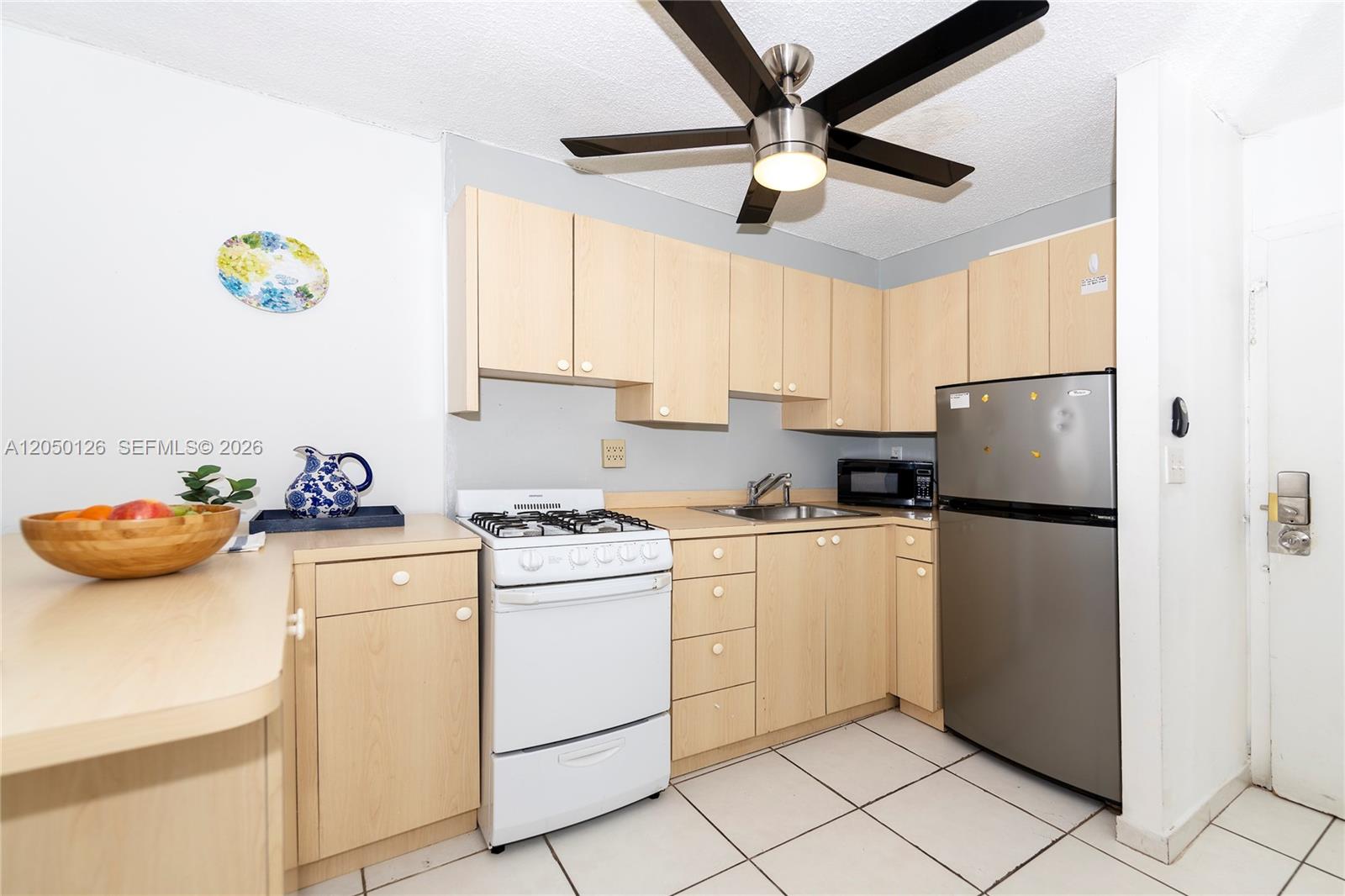 A small kitchen features light wood cabinets, a white stove, and a stainless steel refrigerator — 710 Washington Ave # 414, Miami Beach FL 33139, MIAMI BEACH, FL