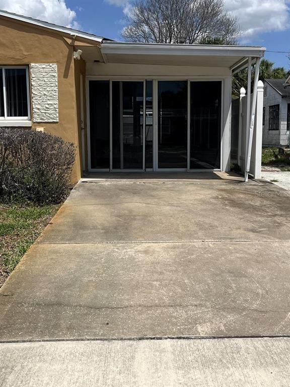 A concrete driveway leads to a covered patio with sliding glass doors on a house — 360 72ND AVENUE, ST PETERSBURG, FL