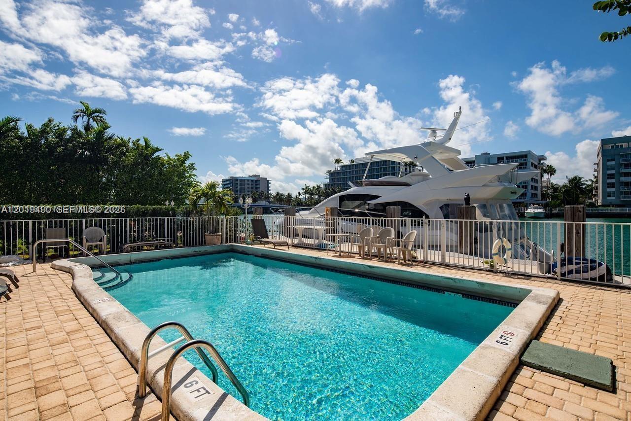 A rectangular swimming pool sits on a patio overlooking a docked yacht and waterway — 34 Bal Bay Dr, Bal Harbour FL 33154, BAL HARBOUR, FL