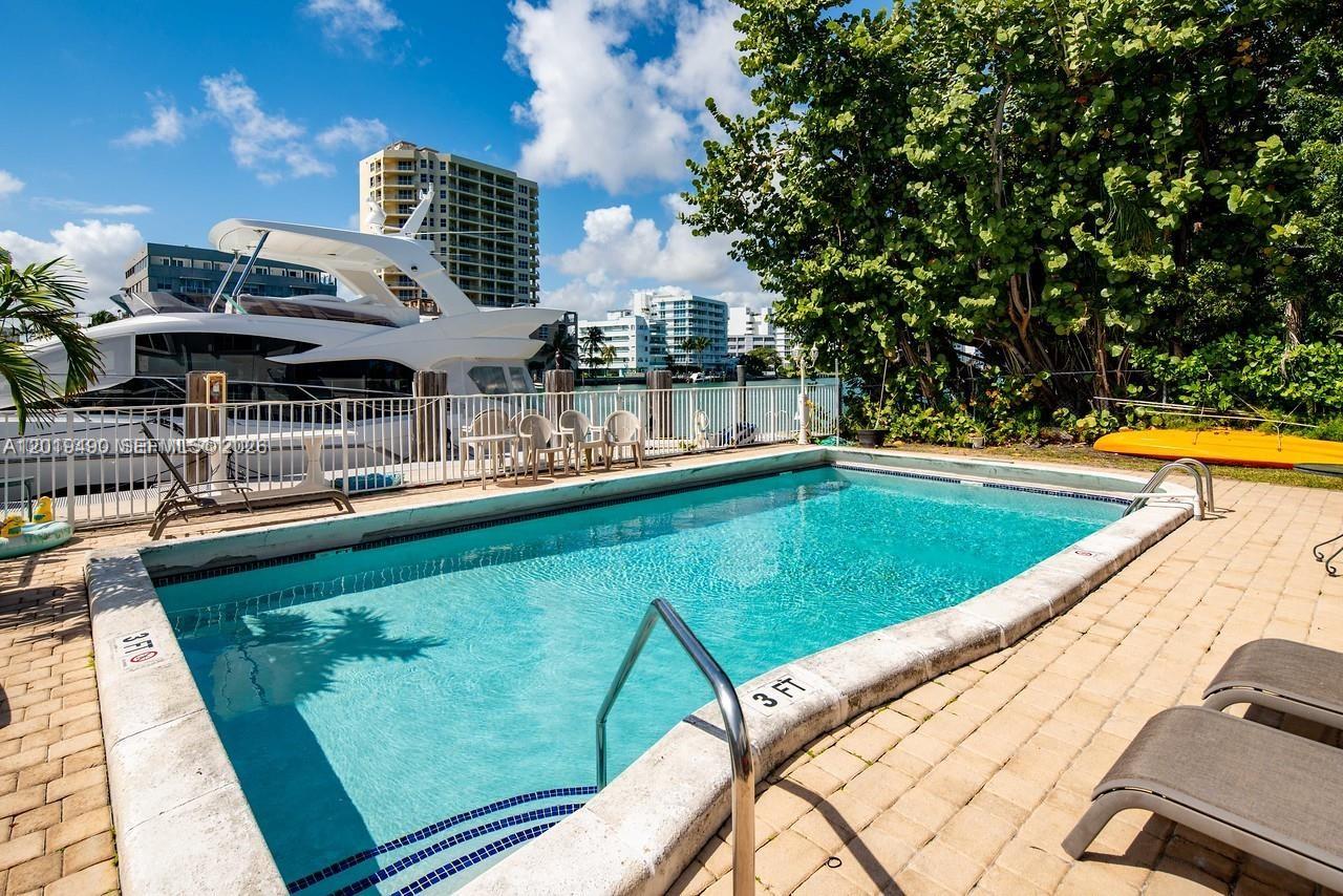 A rectangular swimming pool sits on a paved patio next to a large yacht — 34 Bal Bay Dr, Bal Harbour FL 33154, BAL HARBOUR, FL