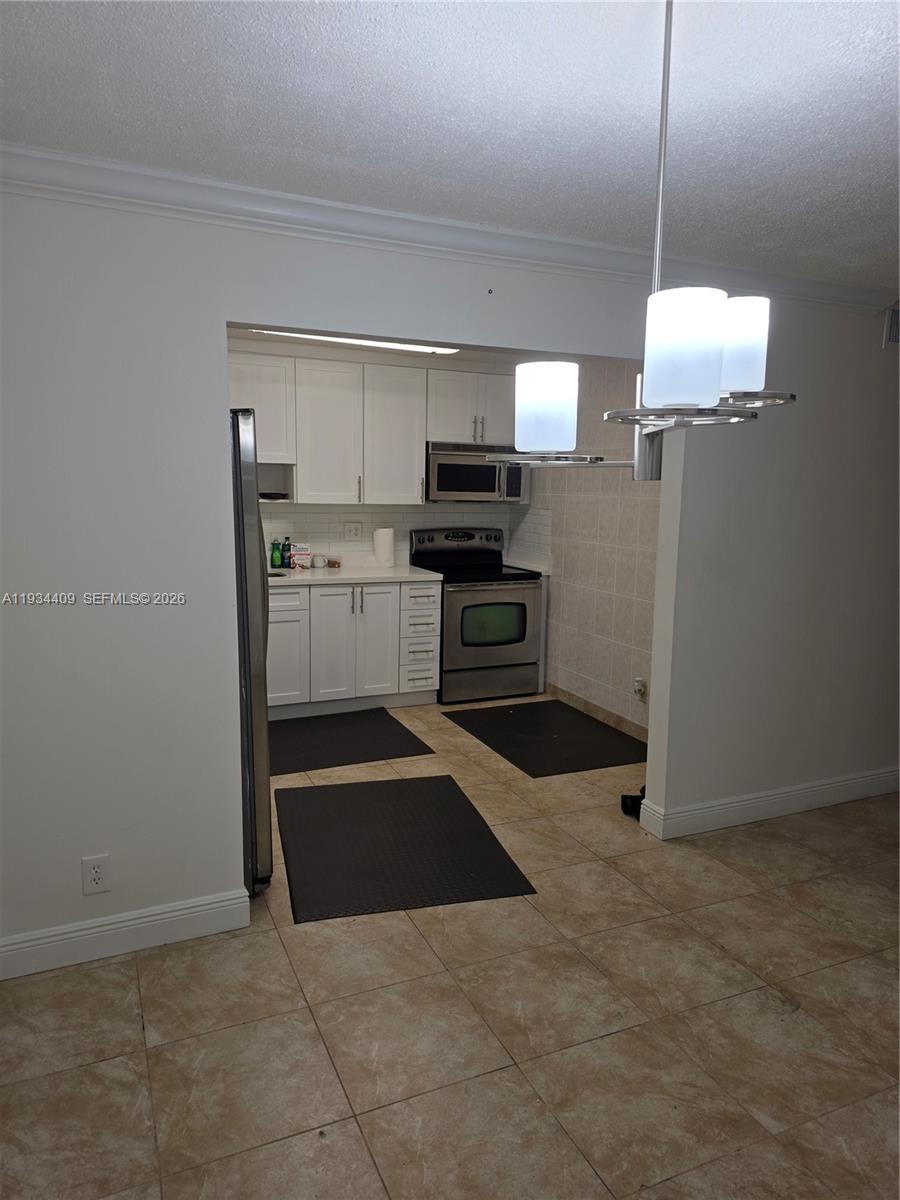 A kitchen with white cabinets, stainless steel appliances, and tile flooring is viewed from an adjacent room — 1811 Jefferson St # 501, Hollywood FL 33020, HOLLYWOOD, FL