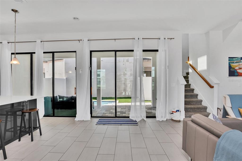 A bright living room features tile floors, sliding glass doors to a pool, and stairs — 407 VILLA DOMANI WAY, DAVENPORT, FL