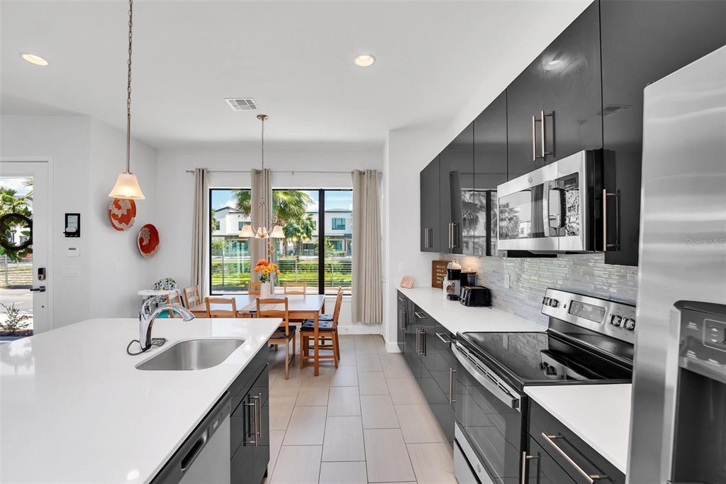 A modern kitchen features dark glossy cabinets, white countertops, stainless steel appliances, and a dining area — 407 VILLA DOMANI WAY, DAVENPORT, FL