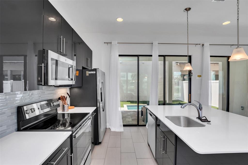A modern kitchen features dark cabinetry, white countertops, stainless steel appliances, and sliding glass doors — 407 VILLA DOMANI WAY, DAVENPORT, FL