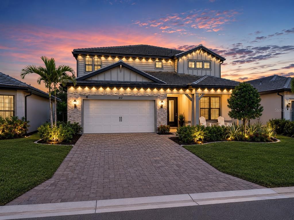 A two-story house with a stone facade, paved driveway, and exterior accent lighting at dusk — 812 GADWALL COURT, BRADENTON, FL