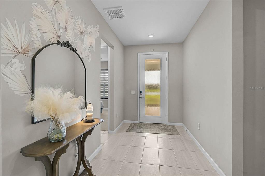 A bright entryway features a console table, a decorative mirror, and a glass-paneled front door — 812 GADWALL COURT, BRADENTON, FL