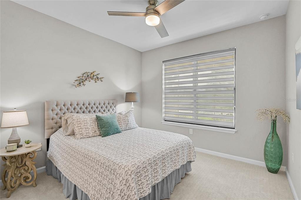 A bedroom features a tufted headboard, a ceiling fan, and a window with striped shades — 812 GADWALL COURT, BRADENTON, FL