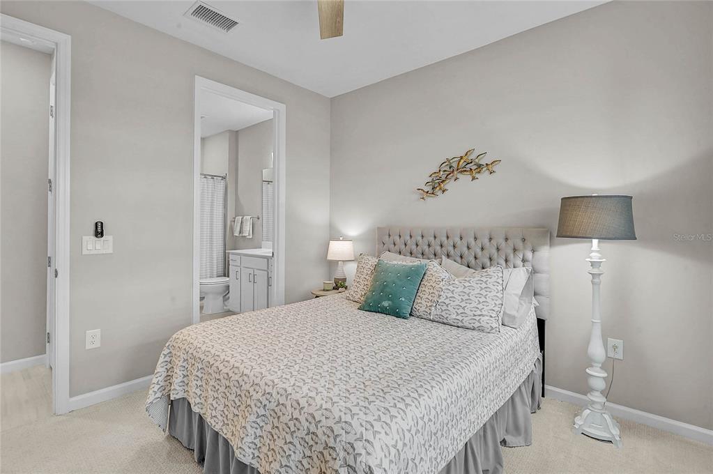 A bedroom with a tufted headboard, patterned bedding, and an attached bathroom — 812 GADWALL COURT, BRADENTON, FL