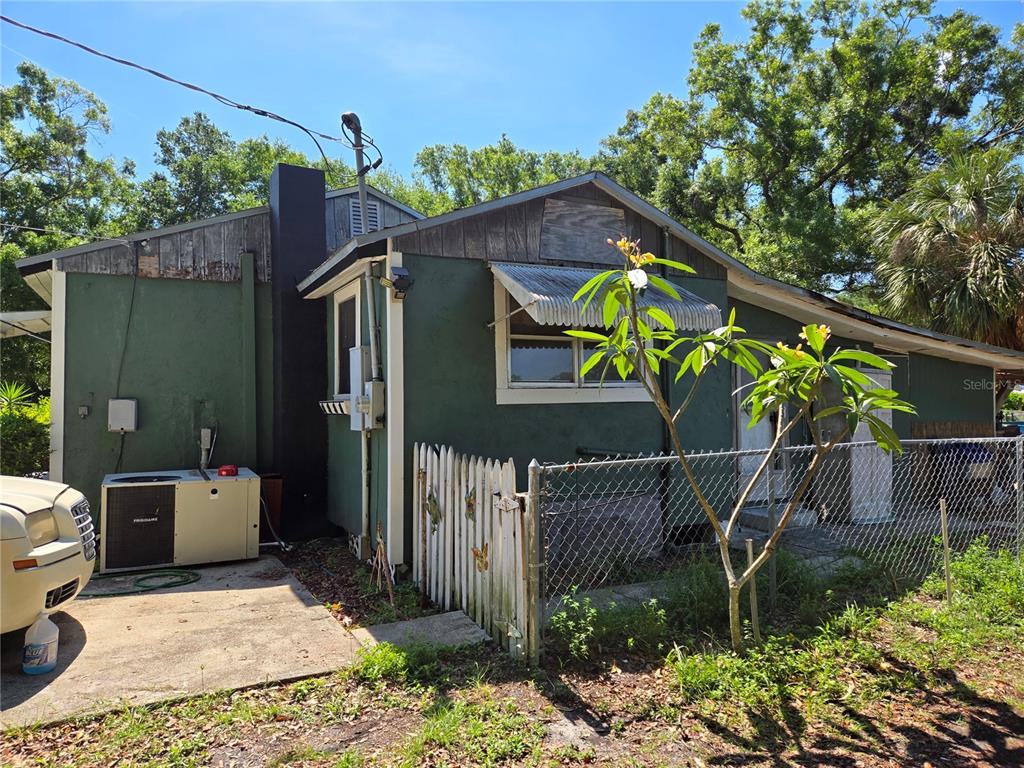 The exterior of a green house with a metal awning, chain-link fence, and HVAC unit — 2010 W JEAN STREET, TAMPA, FL
