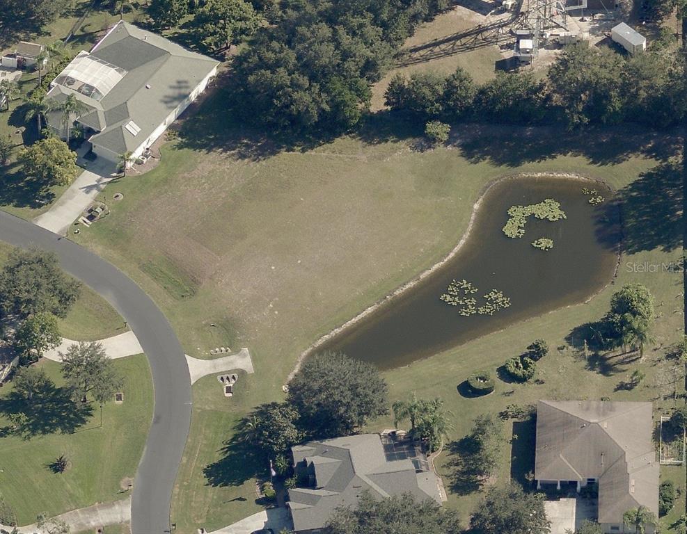 An aerial view shows a vacant residential lot with a pond next to two houses — 19915 DOLORES ANN COURT, LUTZ, FL