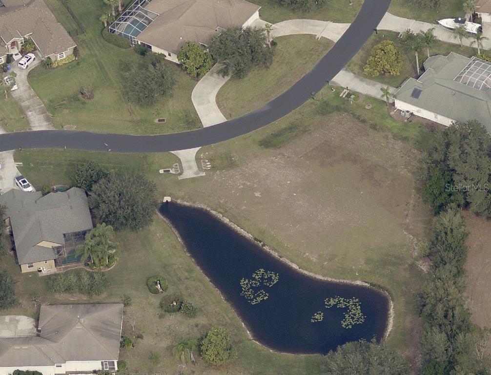 An aerial view shows a vacant residential lot featuring a pond and surrounding houses — 19915 DOLORES ANN COURT, LUTZ, FL
