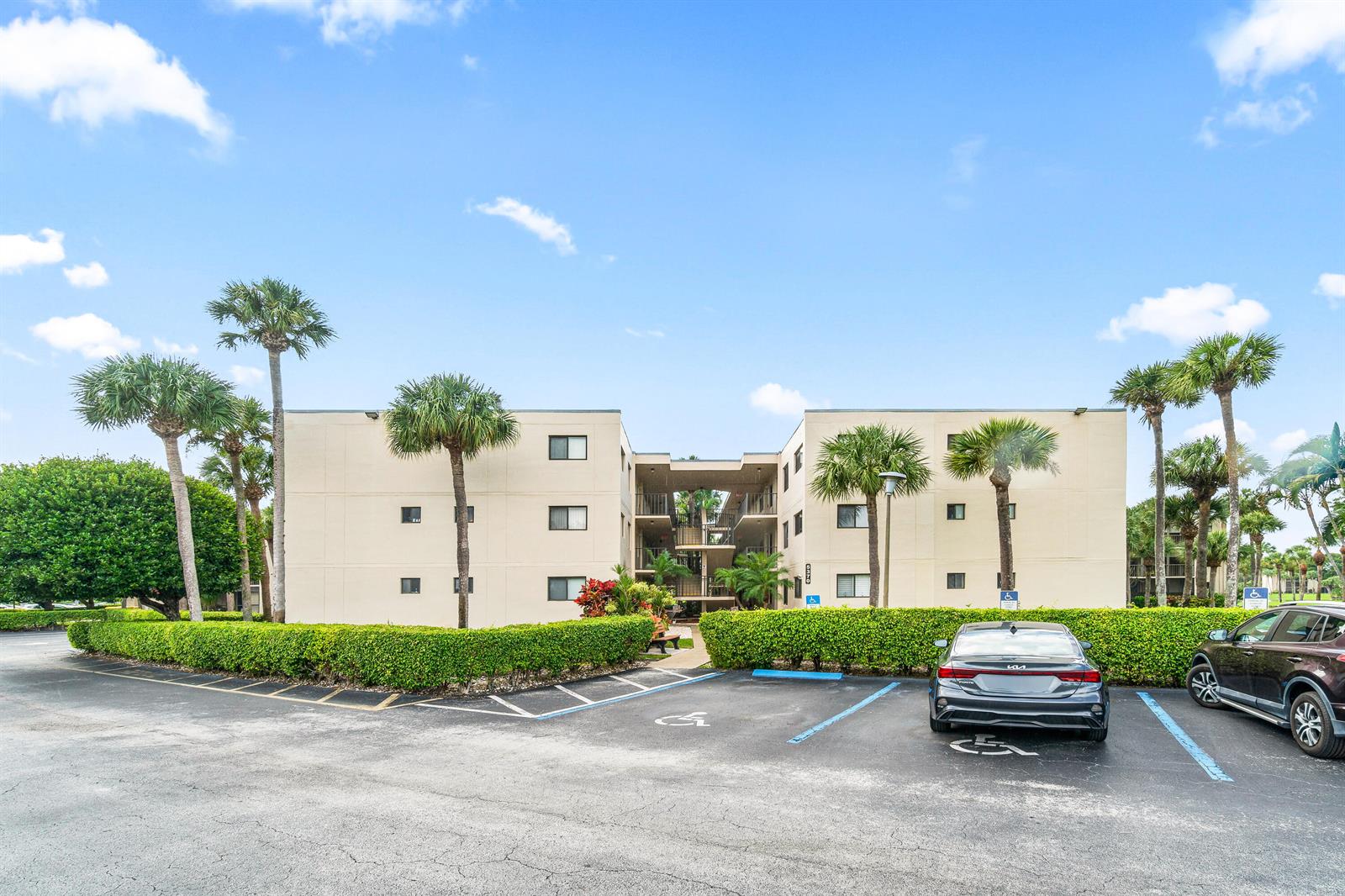A three-story apartment building with palm trees and a parking lot in the foreground — 5370 Las Verdes Circle # 209, Delray Beach FL 33484, DELRAY BEACH, FL