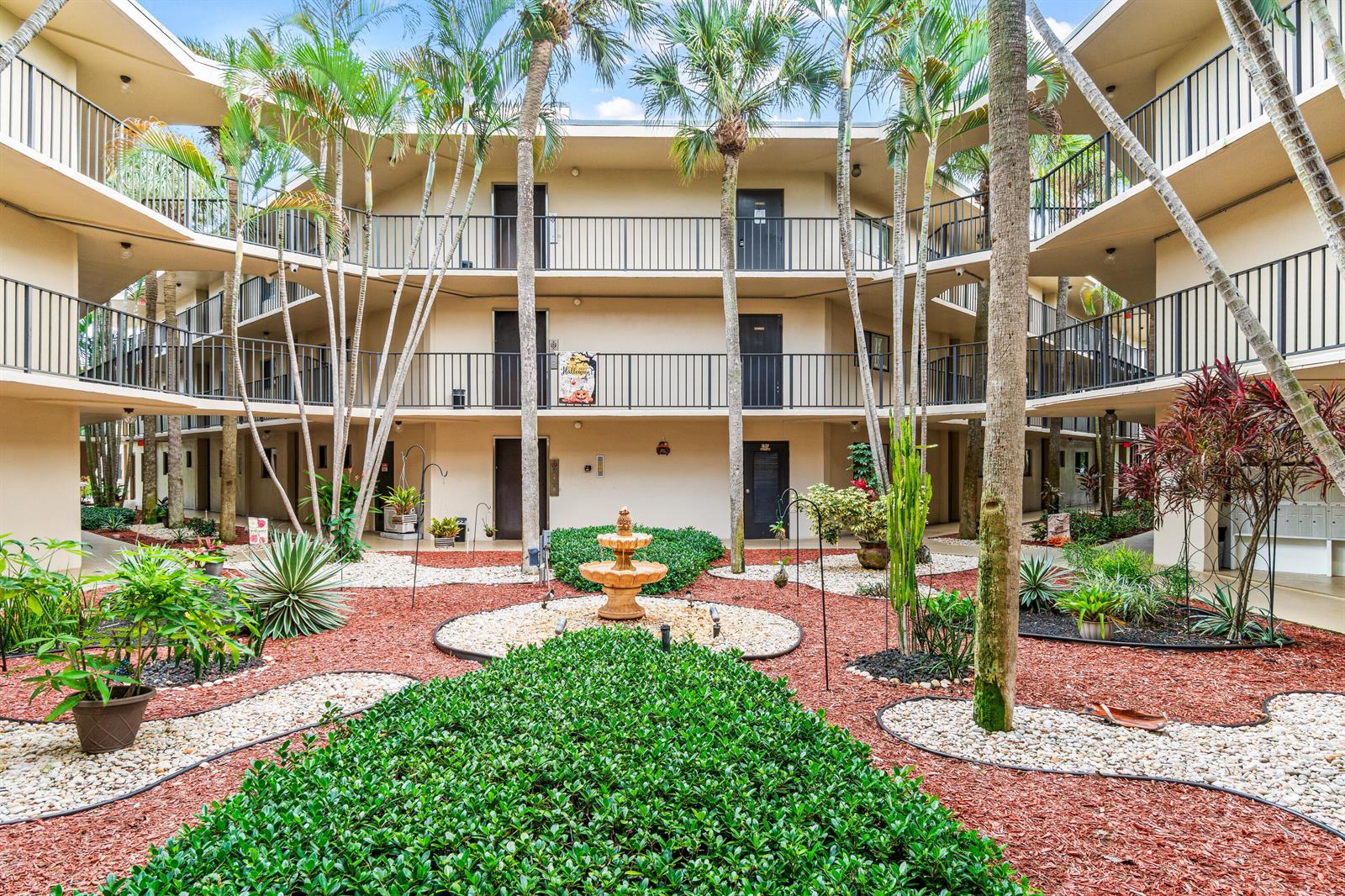 A courtyard with a central fountain, palm trees, and landscaping surrounded by a multi-story apartment building — 5370 Las Verdes Circle # 209, Delray Beach FL 33484, DELRAY BEACH, FL