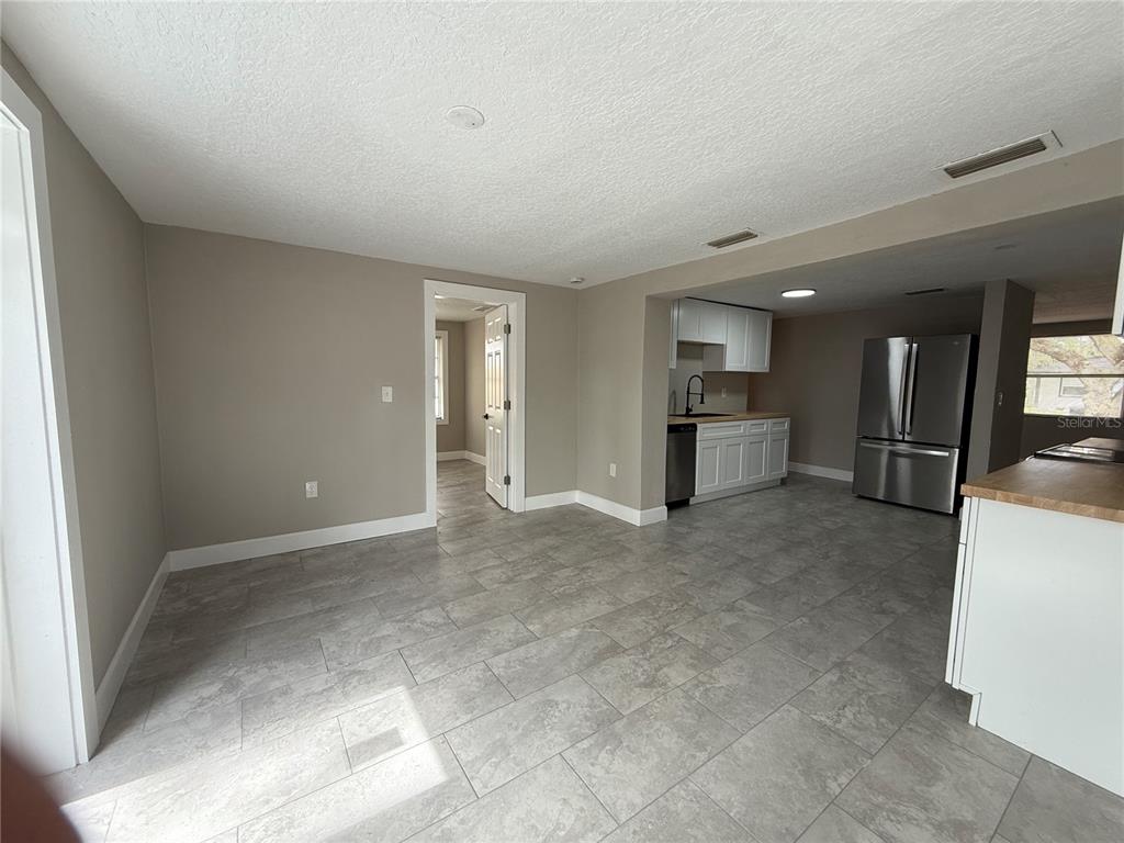 A kitchen with stainless steel appliances and white cabinets opens into a tiled dining area — 7138 PINEWOOD DRIVE, NEW PORT RICHEY, FL