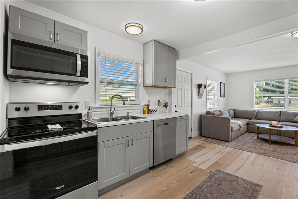 A kitchen with grey cabinets and stainless steel appliances opens into a living room area — 204 6TH AVENUE NW, RUSKIN, FL