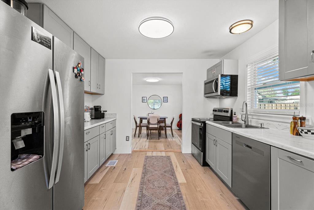 A kitchen with gray cabinets, stainless steel appliances, and wood-look flooring leads to a dining area — 204 6TH AVENUE NW, RUSKIN, FL