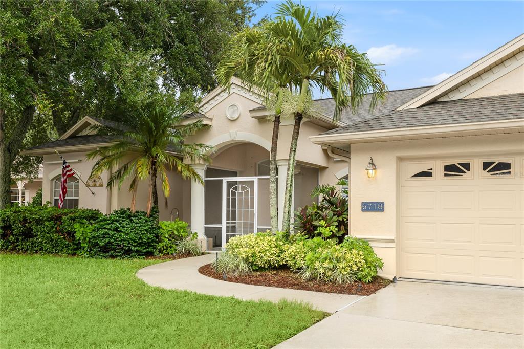 The exterior of a beige house features a screened front door, columns, and palm trees — 6718 WILLOW POND LANE, SARASOTA, FL