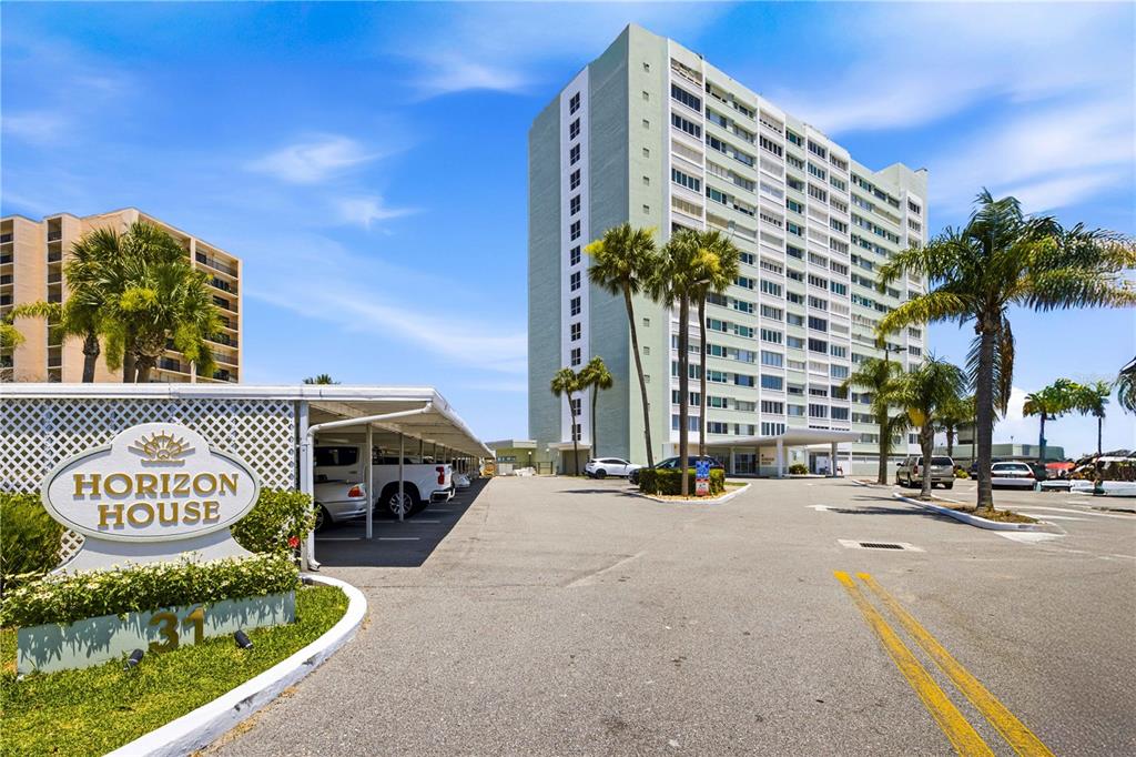 The exterior of a tall, light-colored apartment building with a parking lot and signage — 31 ISLAND WAY UNIT 1404, CLEARWATER, FL