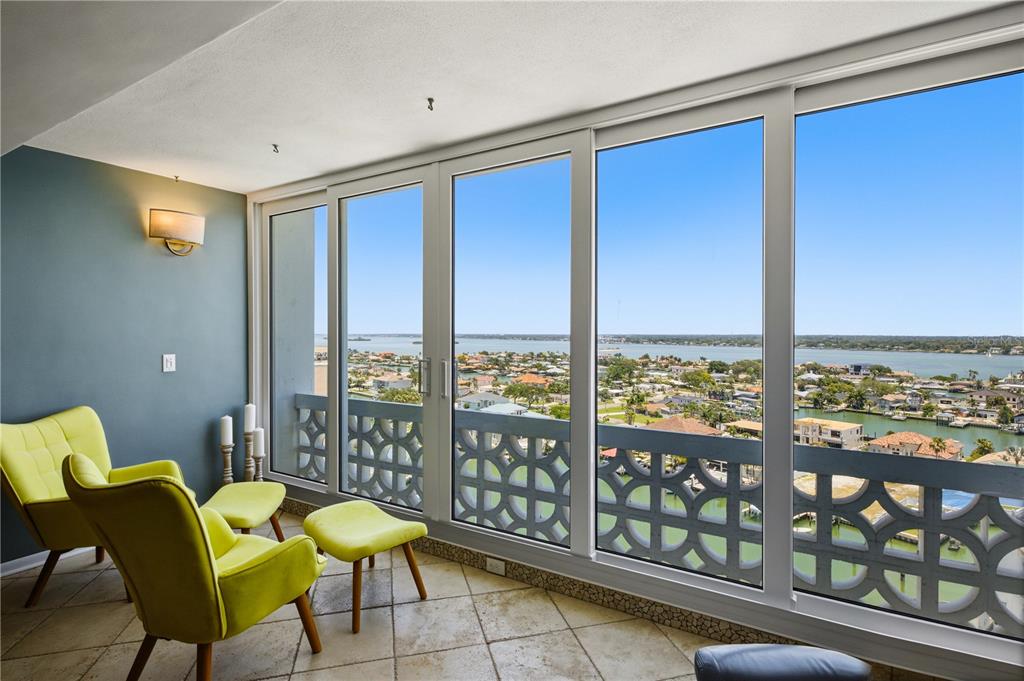 A sunroom with tile floors, lime green chairs, and large windows overlooking a waterfront neighborhood — 31 ISLAND WAY UNIT 1404, CLEARWATER, FL