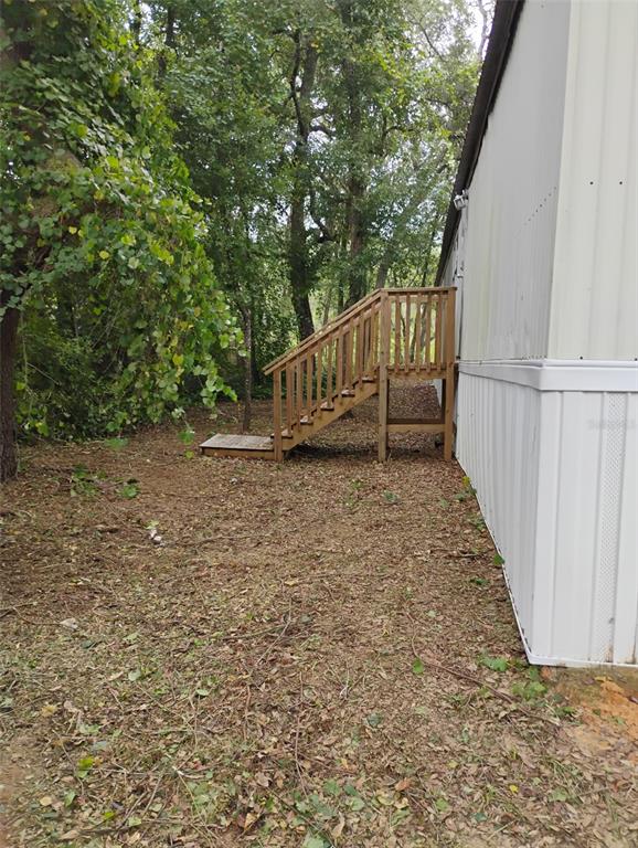 A wooden staircase leads to the side entrance of a mobile home near wooded trees — 6364 SWARTHMORE DRIVE, KEYSTONE HEIGHTS, FL