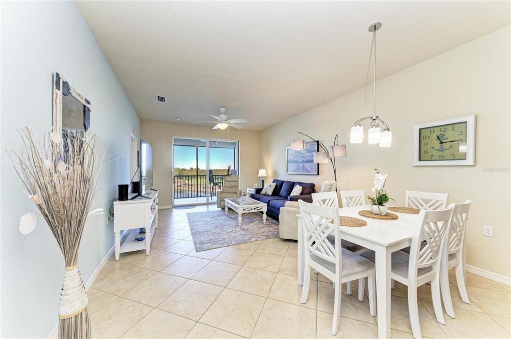 An open-concept living and dining area features tile flooring, a white dining set, and balcony access — 7911 GRAND ESTUARY TRAIL UNIT 403, BRADENTON, FL