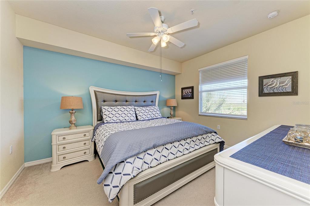 A bedroom features a blue accent wall, a white bed frame, and a ceiling fan — 7911 GRAND ESTUARY TRAIL UNIT 403, BRADENTON, FL