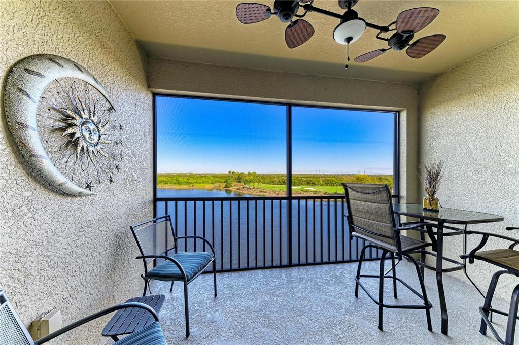 A screened-in balcony features a ceiling fan, outdoor furniture, and a view of a lake — 7911 GRAND ESTUARY TRAIL UNIT 403, BRADENTON, FL