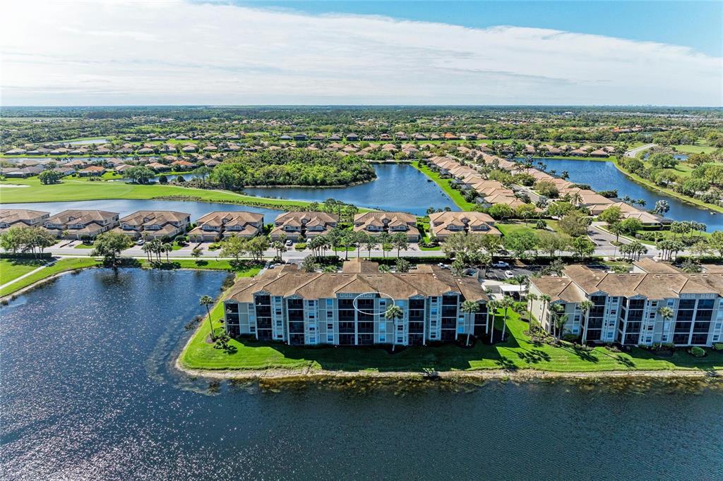 An aerial view shows a multi-story apartment building situated on a waterfront lot — 7911 GRAND ESTUARY TRAIL UNIT 403, BRADENTON, FL