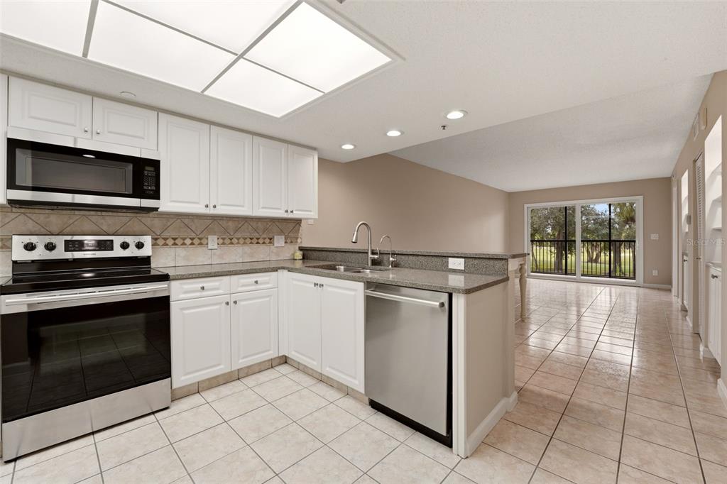 A kitchen with white cabinets, stainless steel appliances, and tile flooring overlooks a living area — 2320 TERRA CEIA BAY BOULEVARD UNIT 207, PALMETTO, FL