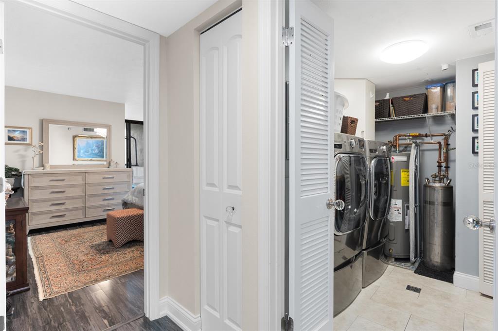 A laundry room with a washer, dryer, and water heater sits beside a bedroom doorway — 1600 GULF BOULEVARD UNIT 717, CLEARWATER BEACH, FL