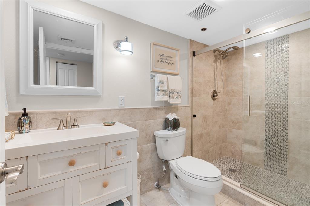 A bathroom features a white vanity, a toilet, and a glass-enclosed shower with tiled walls — 1600 GULF BOULEVARD UNIT 717, CLEARWATER BEACH, FL