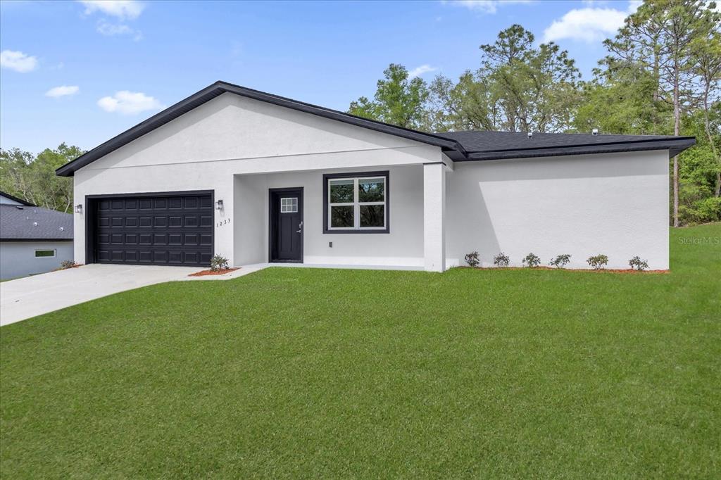 A single-story house with white stucco walls, a black garage door, and a black roof — 1233 W SHADY LANE, DUNNELLON, FL