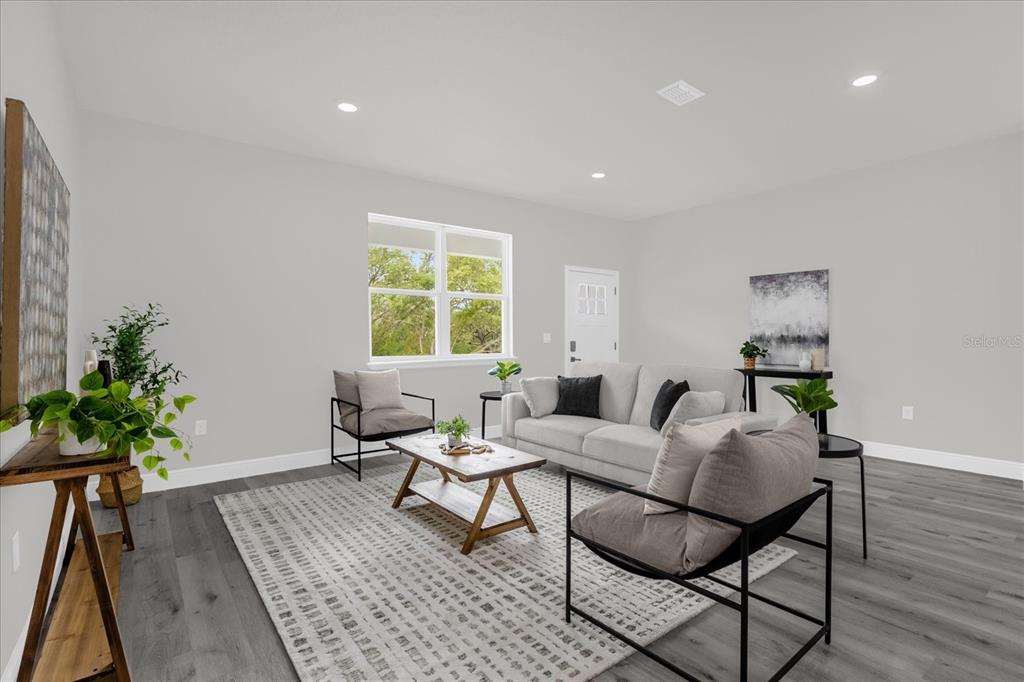 A living room features gray wood-look flooring, a light gray sofa, and two modern chairs — 1233 W SHADY LANE, DUNNELLON, FL