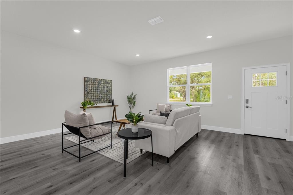 A living room features gray wood-look flooring, a light gray sofa, and a white door — 1233 W SHADY LANE, DUNNELLON, FL