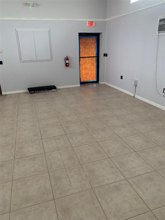 An empty room with light gray walls, tiled flooring, an exit door, and a fire extinguisher — 1221 S MCCALL ROAD UNIT B, ENGLEWOOD, FL