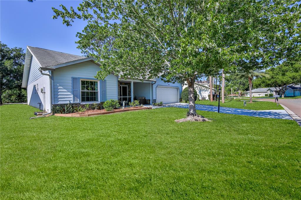 A light blue single-story house with a front lawn, a tree, and a garage — 7088 CROWN OAKS DRIVE, SPRING HILL, FL