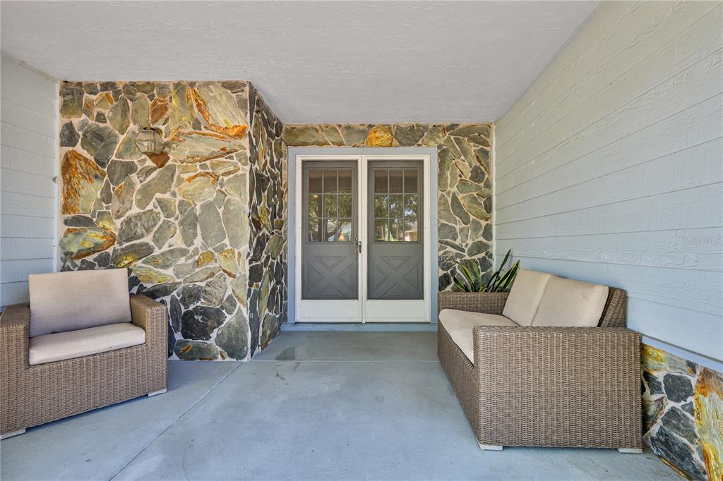 A covered patio features stone walls, light blue siding, and two pieces of wicker furniture — 7088 CROWN OAKS DRIVE, SPRING HILL, FL