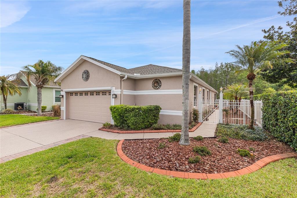 A single-story house with a beige stucco exterior, a two-car garage, and a gated walkway — 8328 PONKAN ROAD, LAND O LAKES, FL
