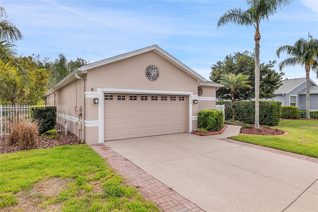 A beige, single-story house features a two-car garage, a concrete driveway, and palm trees — 8328 PONKAN ROAD, LAND O LAKES, FL